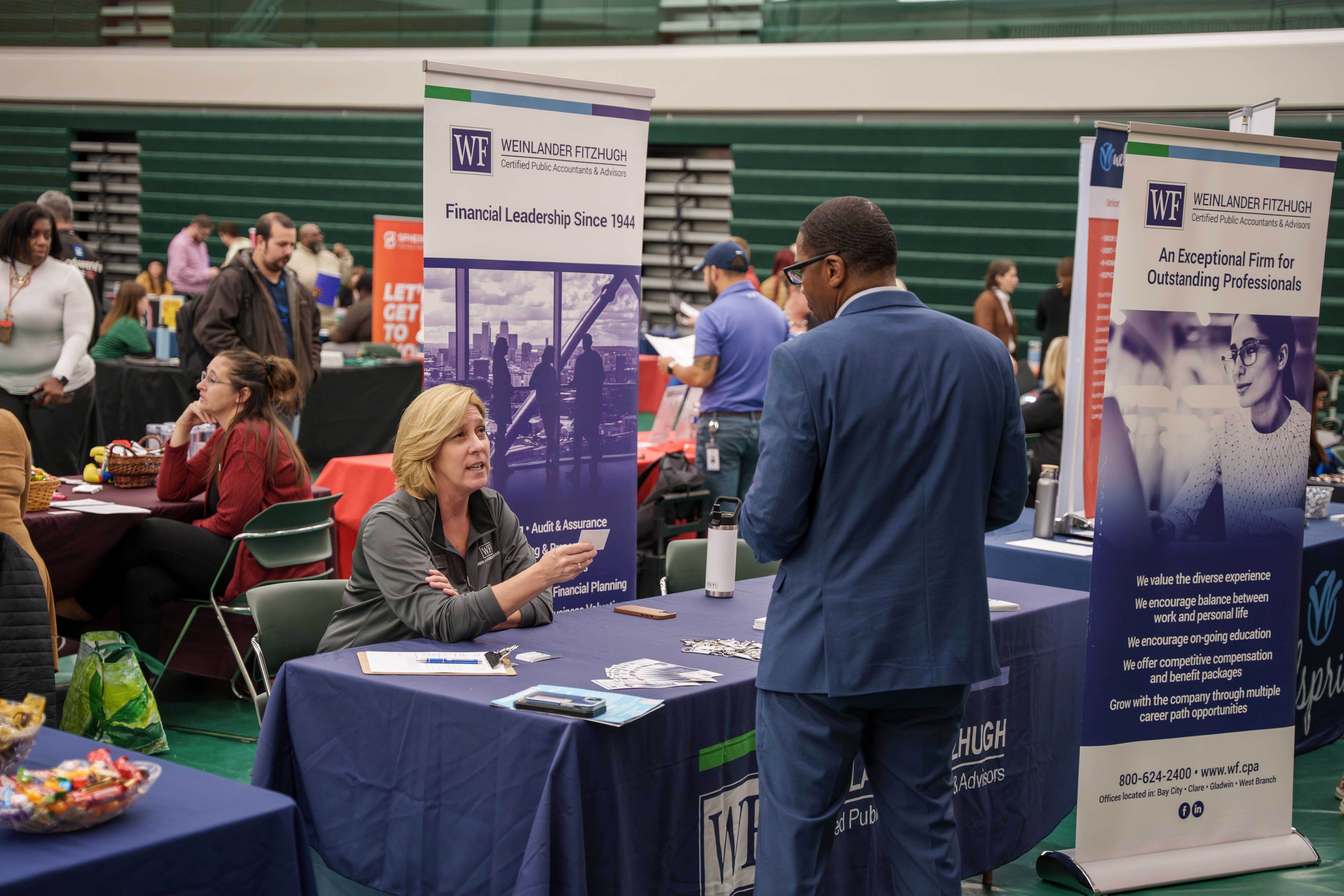 job seeker stands in blue suit speaking to a woman seated at a table