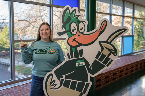 Delta College student posing with Duck mascot cutout
