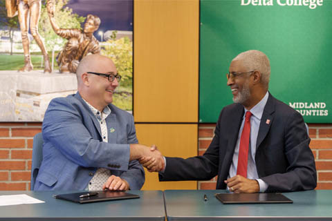 President Gavin of Delta College and President Grant of SVSU sit at a table shaking hands and smiling at each other