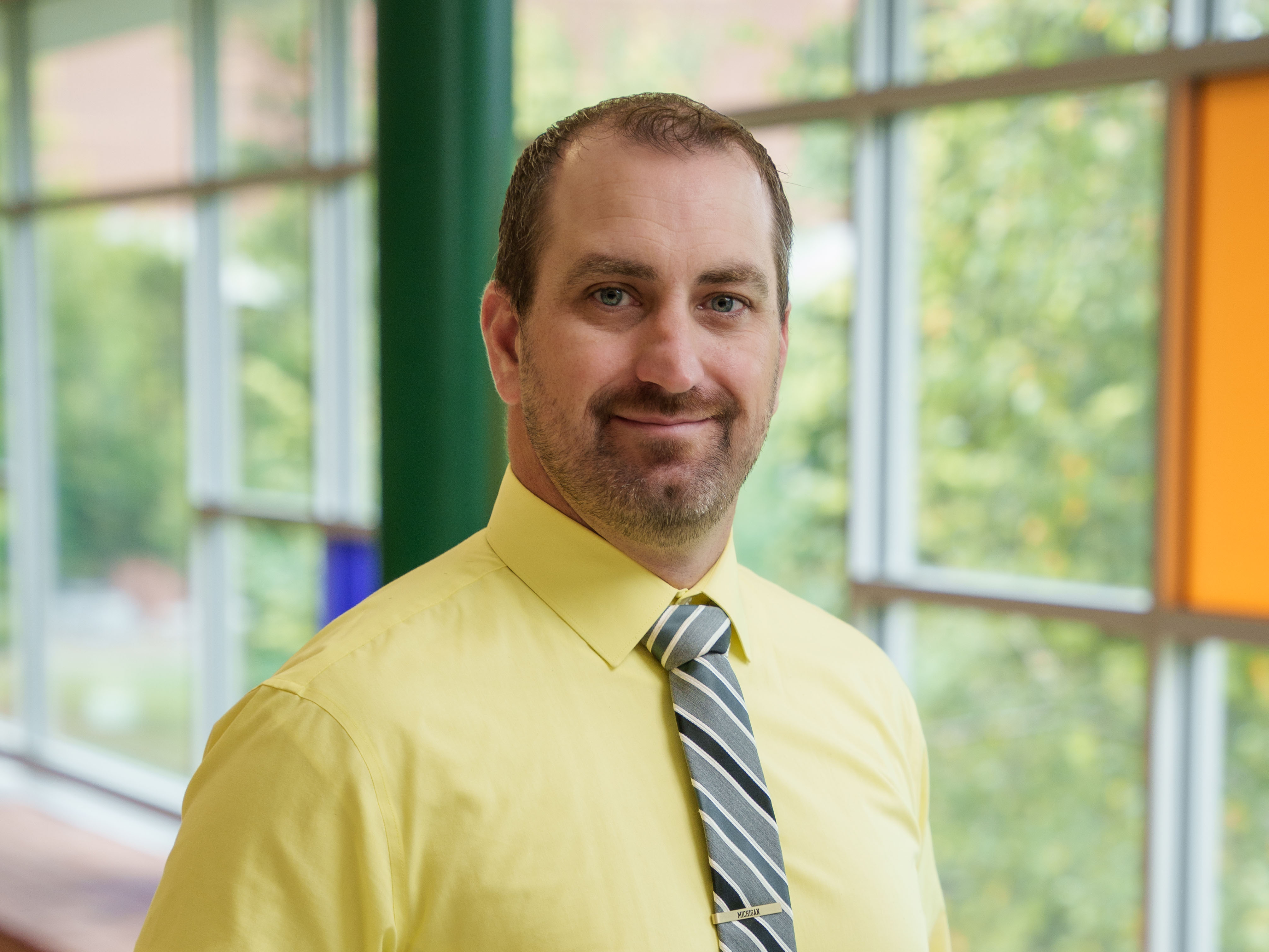 Jon Foco wearing yellow button-up shirt and blue striped tie, smiling for a photo